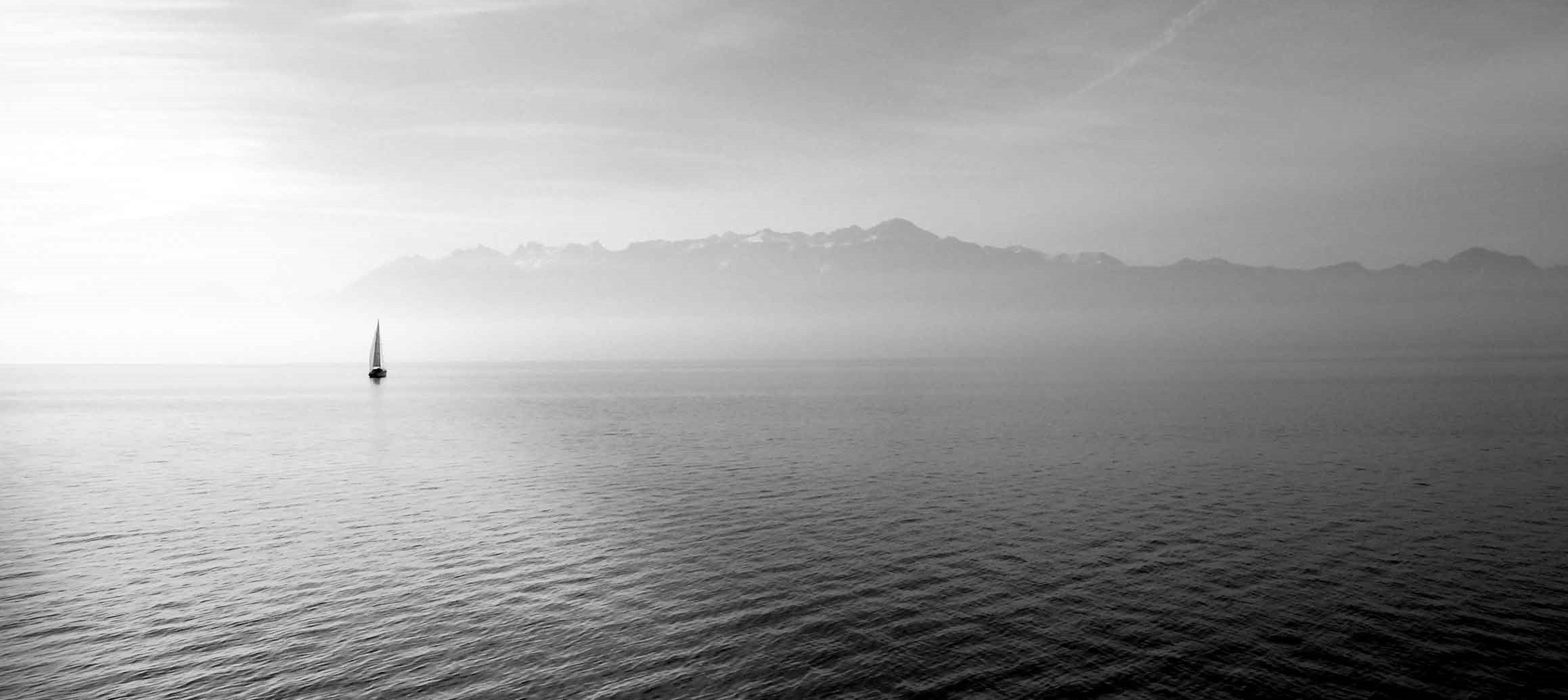 Klein seilboot op 'n rustige meer met berge in die verte